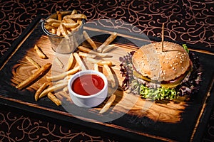 Hamburger with sauce and a bucket of french fries on a wooden plate