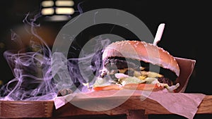 The hamburger is served on a rustic wooden surface and craft paper surrounded by smoke