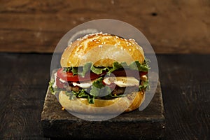 Hamburger on a wooden board against a dark background with copy space. Hamburger with sauce and fresh vegetables on a wooden table