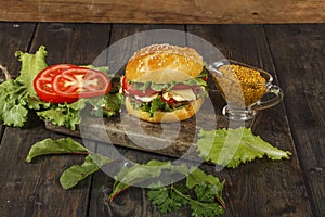 Hamburger on a wooden board against a dark background with copy space. Hamburger with sauce and fresh vegetables on a wooden table