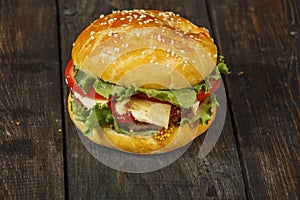 Hamburger on a wooden board against a dark background with copy space. Hamburger with sauce and fresh vegetables on a wooden table