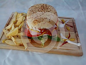 HAMBURGER ON WOODEN TABLE WITH FRIED POTATOES AND SAUCES OF VARIOUS COLORS AND FLAVORS IS A FAST OR CHATARRA FOOD photo