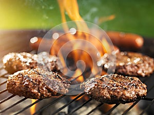 Hamburgers and hotdogs cooking on flaming grill