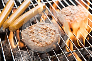 Hamburgers and sausages cooking over flames on grill.