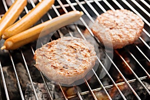 Hamburgers and sausages cooking over flames on grill