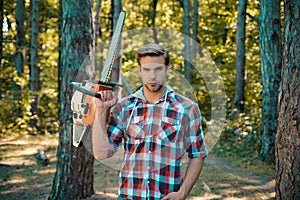 Hamdsome man Lumberjack with an axe or chainsaw in a plaid shirt. Lumberjack with chainsaw in his hands. Stylish young