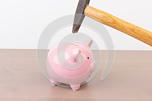 Hammer aiming for pink piggy bank money box on light background. Piggy bank  on wooden background, space for text. Finance, saving