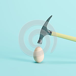 Hammer hitting on a white egg on blue background