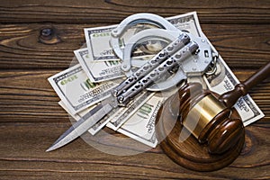Hammer of a judge; knife; handcuffs and money dollars on a wood texture background.