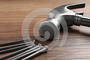 Hammer and metal nails on wooden table, closeup