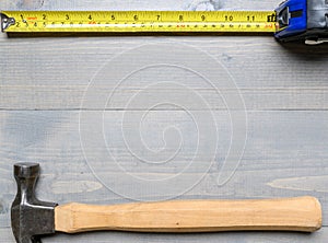 Hammer, nails and a yellow tape measure on wood