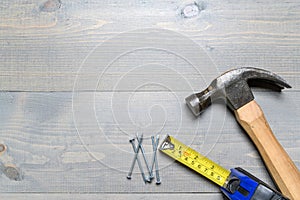 Hammer, nails and a yellow tape measure on wood