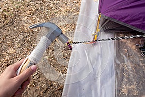 Hammer putting a nail-like tent peg out of iron into the grass on the ground. Push the anchor of the tent onto the ground.Travel