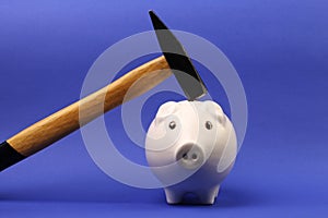Hammer is raised above a upside down white pink piggy bank on blue background