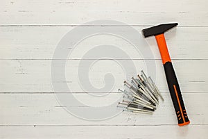 Hammer with a rubberized orange and black handle and stack of dowel nails on white wooden background