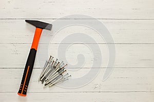 Hammer with a rubberized orange and black handle and stack of dowel nails on white wooden background. Copy space