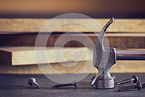 Hammer and screw in lumber stacking background.