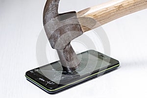 The hammer smashes the smartphone screen lying on the table