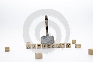 The hammer is standing on the wooden cubes with the word AUTHORITY against white background