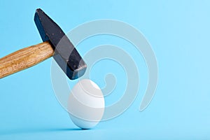 A hammer is about to crush and egg shell on blue background