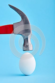 A hammer is about to crush and egg shell on blue background