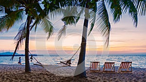 Hammock and beach chairs on the beach with palm trees during sunset at Na Jomtien Beach Pattaya Thailand