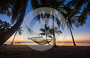 Hammock hanging from coconut palms at sunrise beach