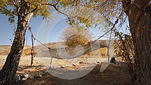 Hammock Hanging Between Two Trees With Dry Summer Landscape With Hills And Yellow Grass On Background