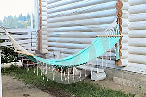 Hammock for relax on backyard outside. Beautiful blue hammock with tassels hanging on log wooden white house. Rest on