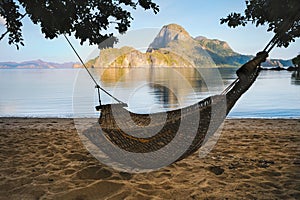 A hammock in the shade with tropical cadlao island in morning light the background