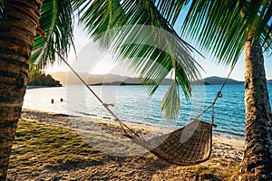 Hammock between two palm trees on the beach at sunset