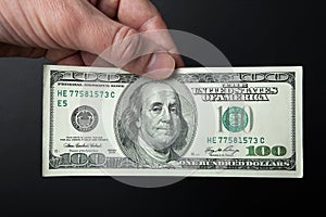 Hand and 100 dollar bill on a black background. Close-up