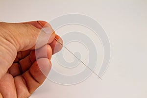 Hand of an acupuncturist holding a long thin acupuncture needle. Man`s hand and metal needle