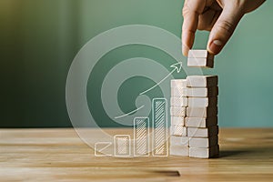 Hand adding block to growing stack with rising bar graph illustration on soft green background