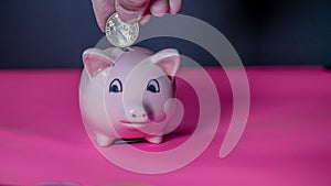 Hand is adding money inside piggy saving bank