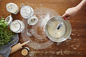 Hand adds ingeredients with spoon into bowl flour dough