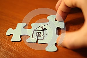 Hand adds puzzle pieces to house closeup. Build house concept. Home comfort and love.