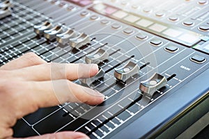 Hand adjusting audio mixer console buttons, faders and sliders.