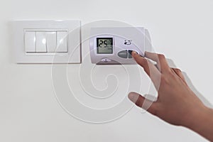 Hand adjusting the heating temperature. Digital thermostat on the wall of the house