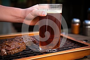 hand adjusting a hot grill, amber ale in a pint glass set to the side