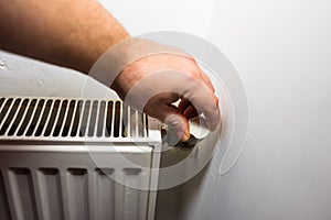 Hand adjusting thermostat valve of heating radiator in a room. Close up heating radiator. Central heating concept, radiator heater