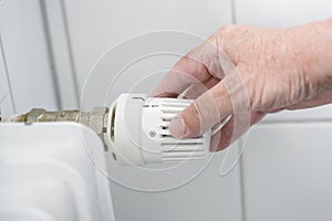 Hand adjusts the thermostat on the heater, the energy crisis with rising prices forces to reduce the heat, copy space, selected