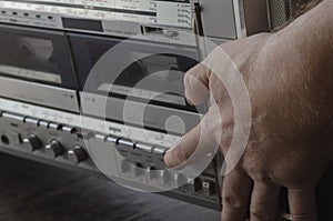 The hand of an adult Caucasian male presses a button on the control panel of a retro stereo cassette recorder