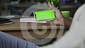 Hand of African American man scrolling web pages on horizontally Smartphone with green screen