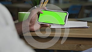 Hand of African American man scrolling web pages on horizontally Smartphone with green screen