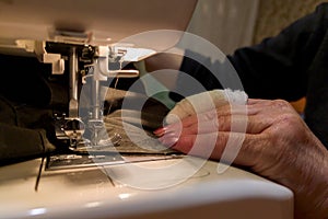 A hand of aged womans with a bandaged finger sews with a sewing machine