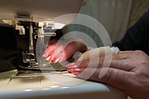 A hand of aged womans with a bandaged finger sews with a sewing machine