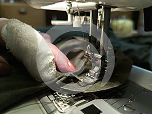 A hand of aged womans with a bandaged finger sews with a sewing machine