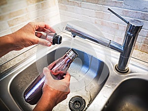 Hand with aluminum eco friendly bottle pour tap water from the sink to reduce plastic usage