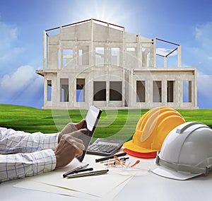 Hand of architect working on computer tablet and house construc